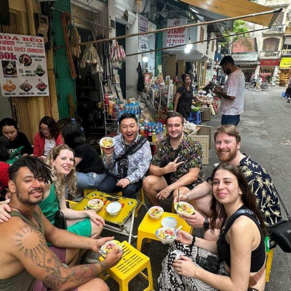 Guests sitting on small stools enjoying Hanoi street food on a lively sidewalk.
